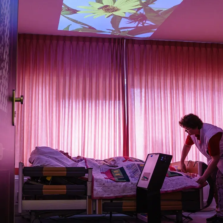 Een cliënt en zorgverlener kijken samen naar een projectie van de Qwiek.up.